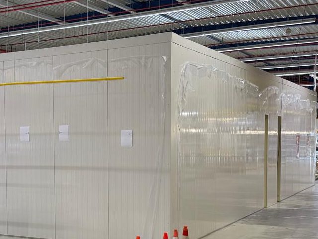 Lange Aussenwand einer Kühlzelle aus weissen Paneelen in einer Lagerhalle, noch mit Schutzfolie