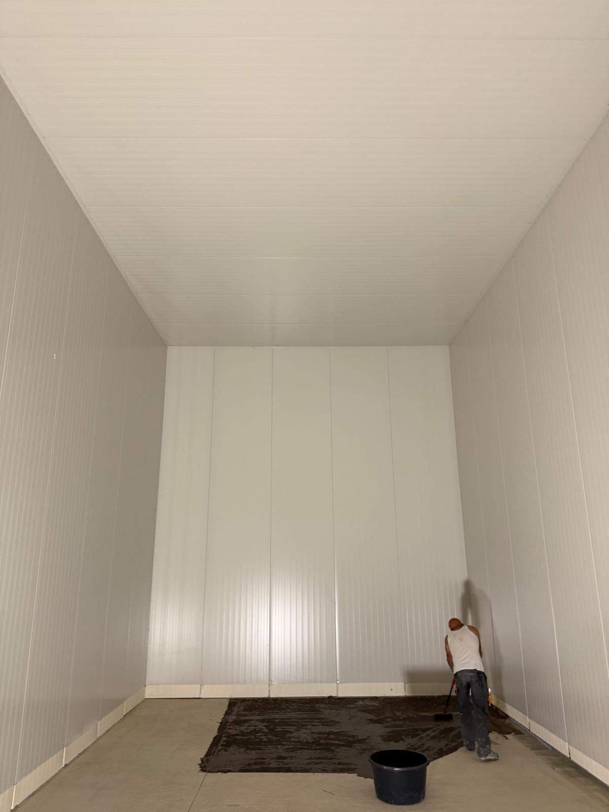Leerer Innenraum einer Kühlzelle mit weissen Wand- und Deckenpaneelen während des Ausbaus